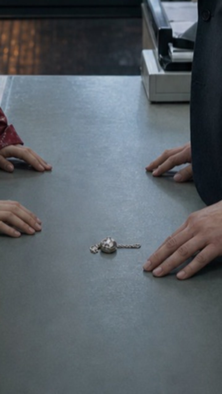 Deterministic crop of the same source still centered on the silver locket and both characters' hands